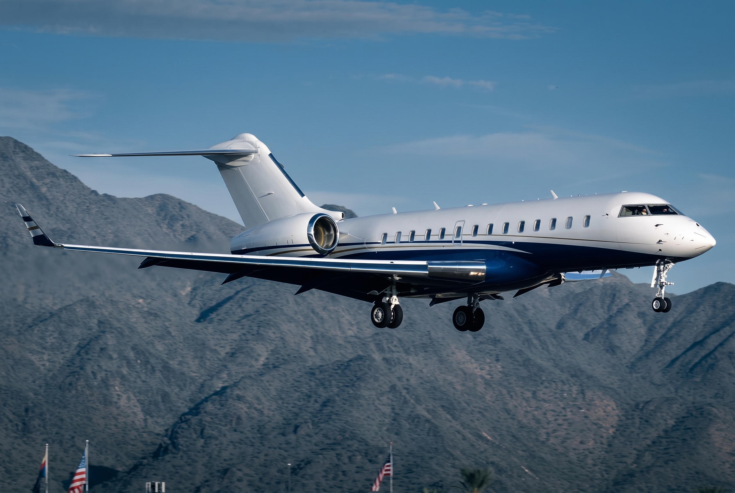 Navy and white large-cabin business jet on final approach against mountain terrain